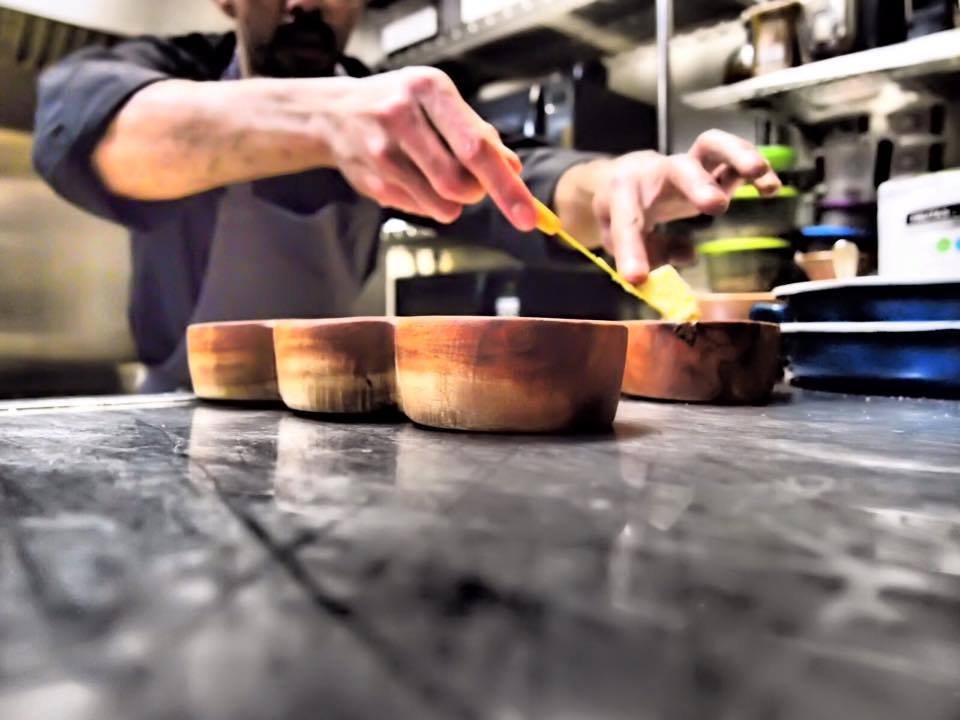 Cocinero termina una preparación en recipientes de madera dentro de la cocina